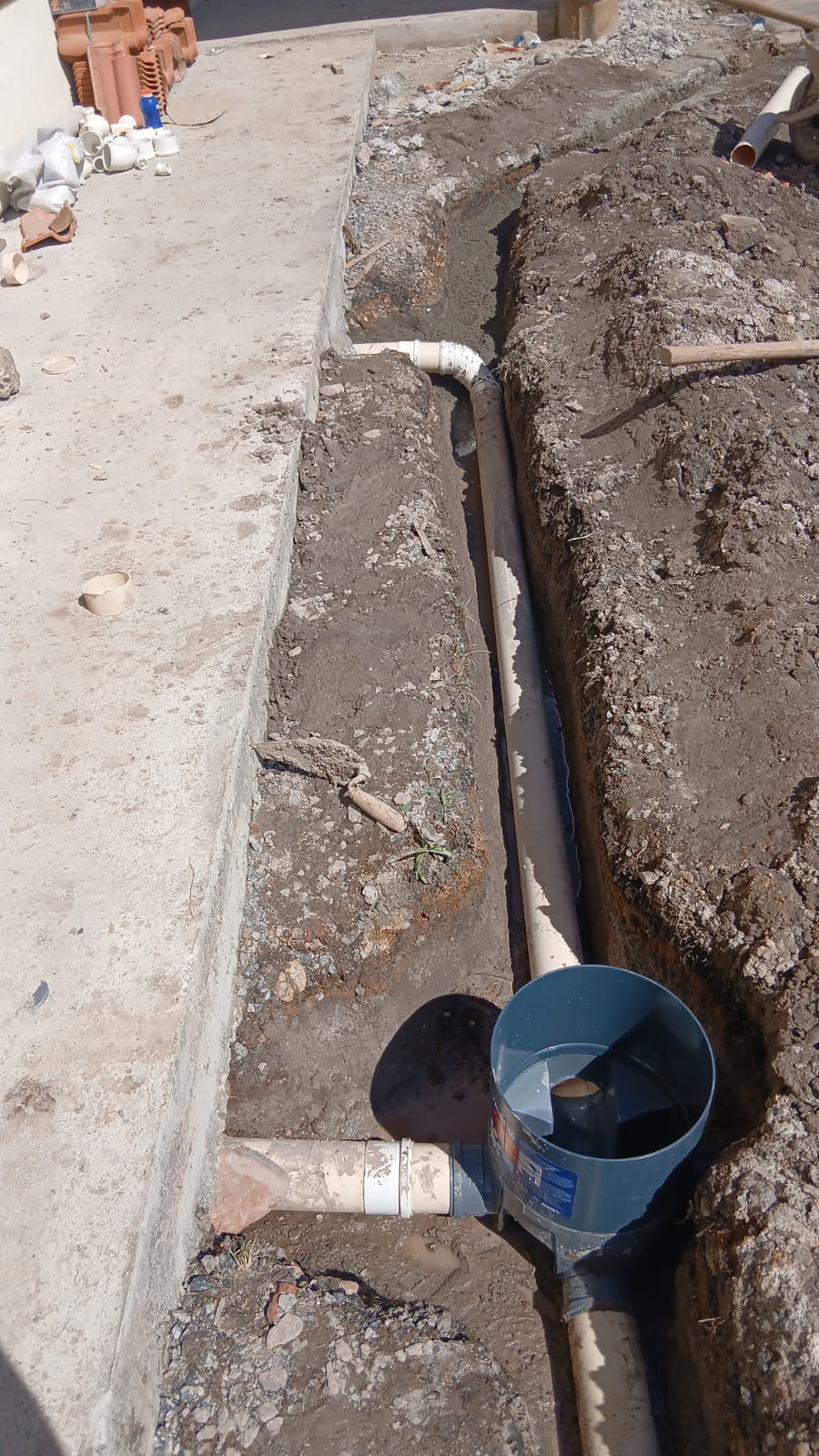 Tubulação em vala aberta conectada a uma caixa de inspeção ao lado de uma construção.